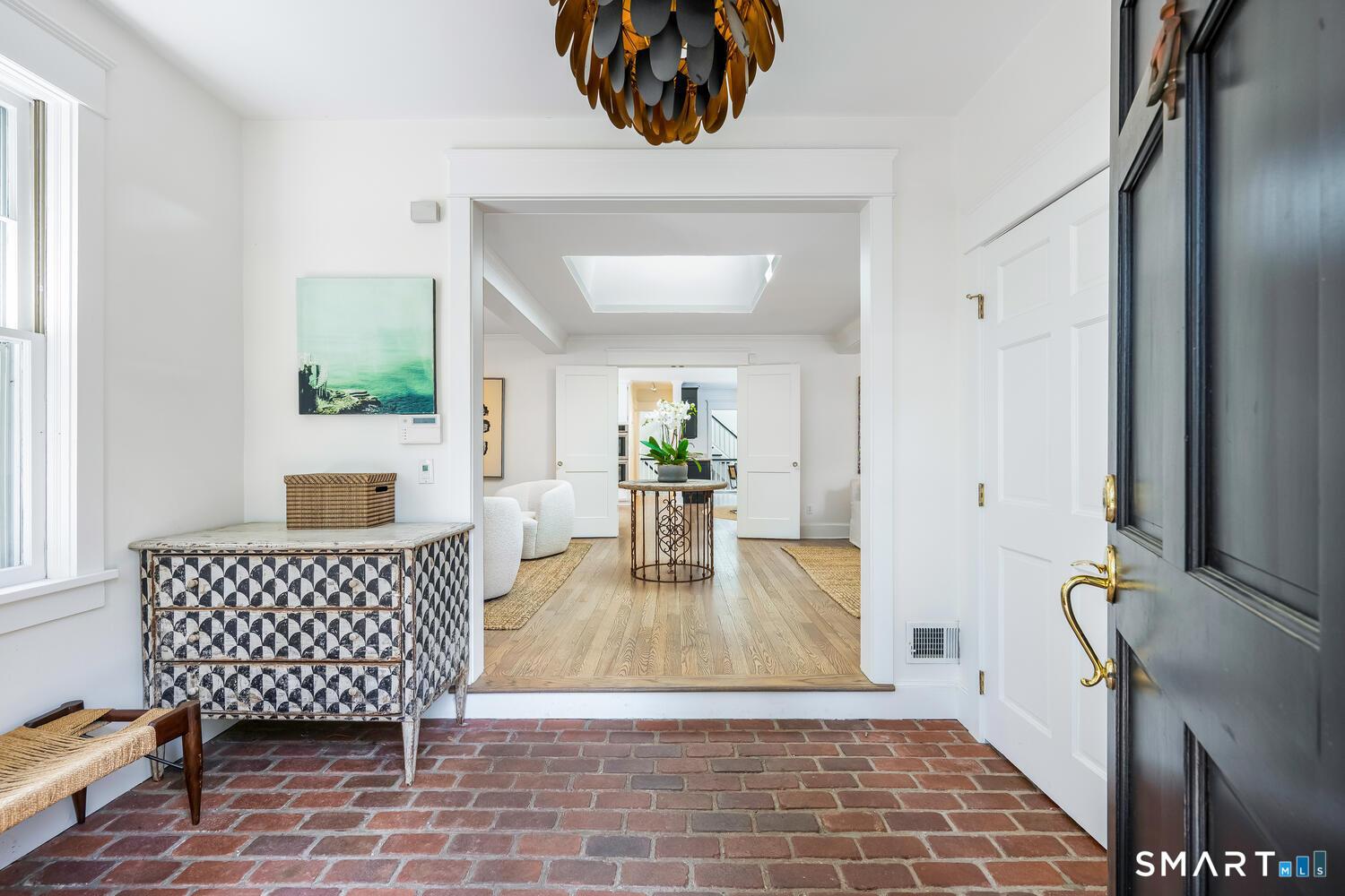 Image 2Front Door: Welcoming grand foyer with classic brick floors, soaring ceiling, statement pendant chandelier, and open sight lines into the home's elegant living spaces.