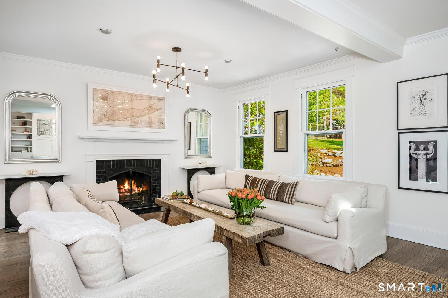 Image 3Living Room: Sun-drenched formal living room showcasing a wood-burning fireplace, coffered ceiling, wide-plank hardwood floors, oversized windows, and designer lighting.
